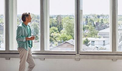 A man stands by a window, gazing thoughtfully outside into the distance.