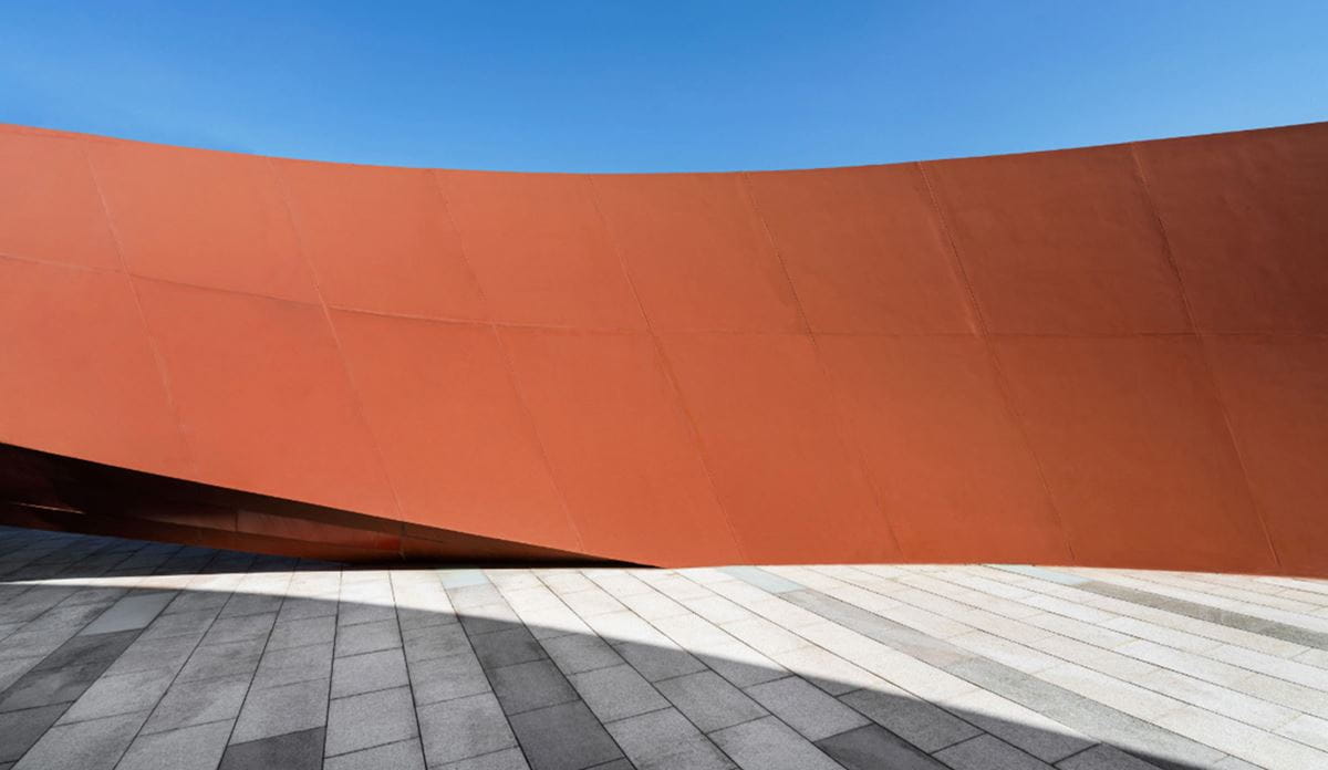 The exterior of a building features a striking red curved wall, emphasizing its unique structure.