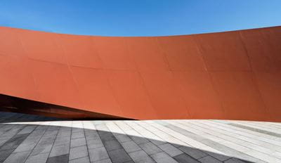 The exterior of a building features a striking red curved wall, emphasizing its unique structure.