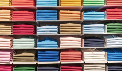 Colorful folded fabrics on screen with two monk figurines on desk.