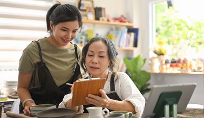 Two women in aprons looking at a tablet together in a modern kitchen