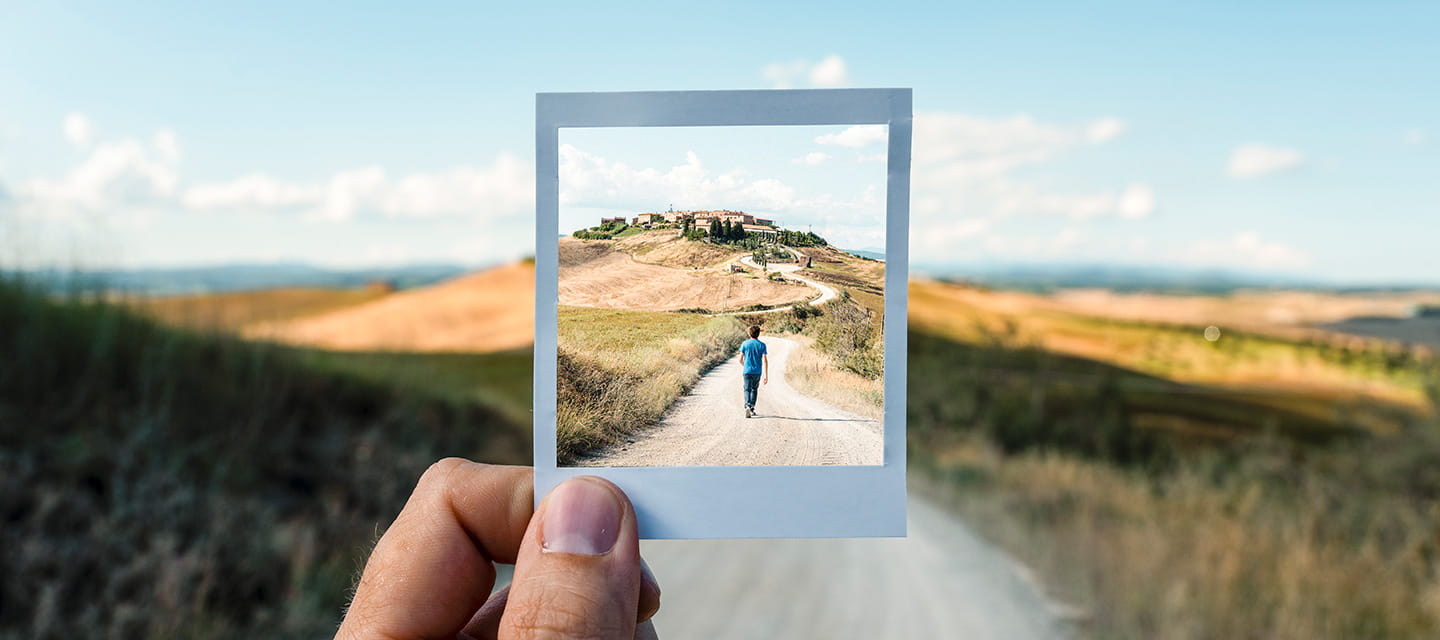 A person holds a photo depicting a road leading to a house, showcasing a scenic residential view.
