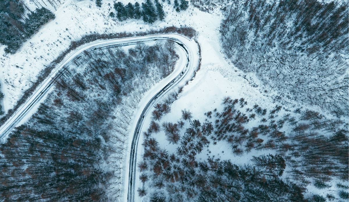 Snow-covered winding road seen from above, illustrating the path through a serene winter landscape.