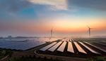 Expansive solar panel field and two wind turbines under a colorful sunrise sky, symbolizing clean energy and sustainability in a serene landscape.