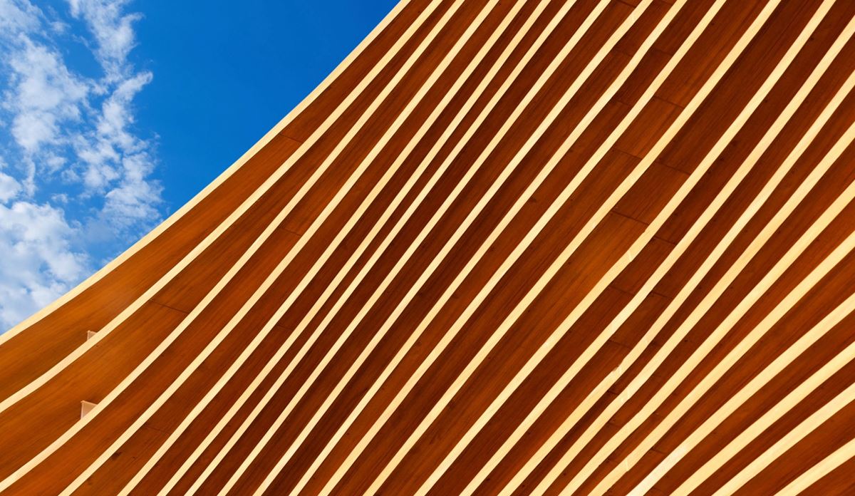 A modern building facade with diagonal white stripes over a reddish-brown surface
