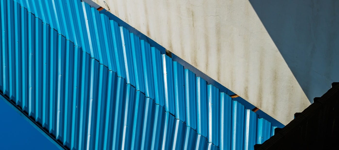 Close-up view of bright blue corrugated metal siding or roofing against a white or cream-colored wall.