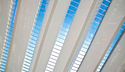 Modern building interior with white structural beams and diagonal glass skylight panels revealing a blue sky