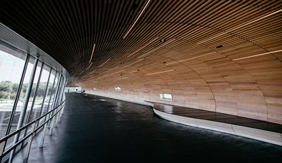 Interior of a modern public infrastructure building featuring curved wooden ceiling panels and floor-to-ceiling glass walls