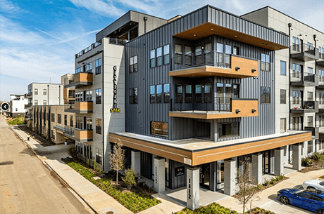 Apartment complex located at the corner of a street, featuring multiple floors and a modern architectural design.
